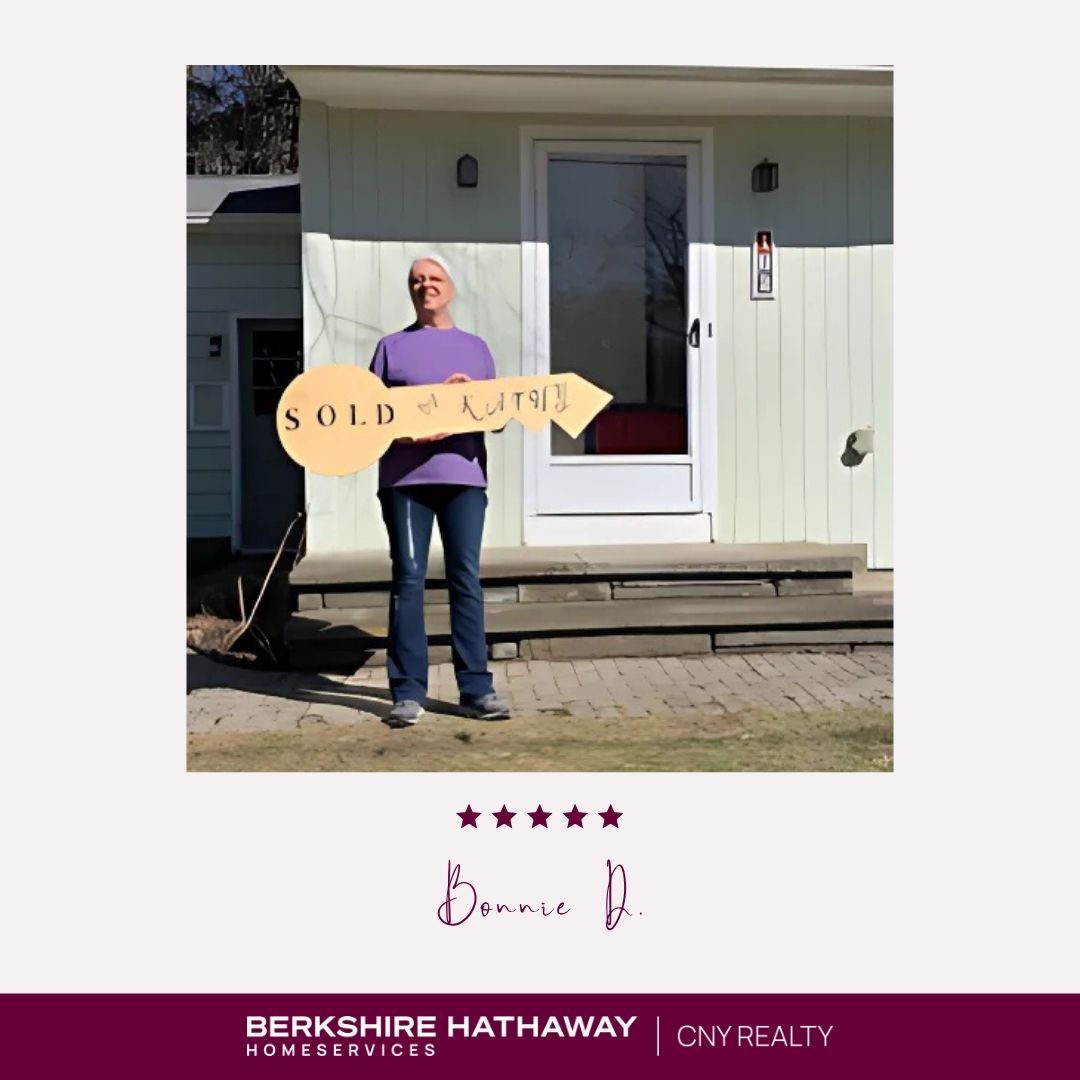 A woman standing in front of a house holding a large key that says "sold by Kathy."