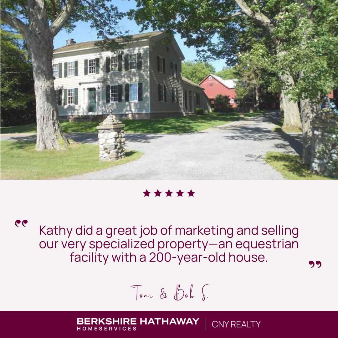 Historic home with stone pillar by driveway and a red barn in the background
